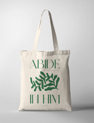 Neutral canvas tote bag featuring green botanical artwork and the uplifting Christian message "Abide in Him" by Littulines, reflecting simple happiness and faith-inspired living.
