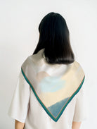  Abstract pastel scarf with teal border worn as a shoulder wrap, featuring soft peach, cream, and blue tones — a faith-forward accessory by The Commandment Co