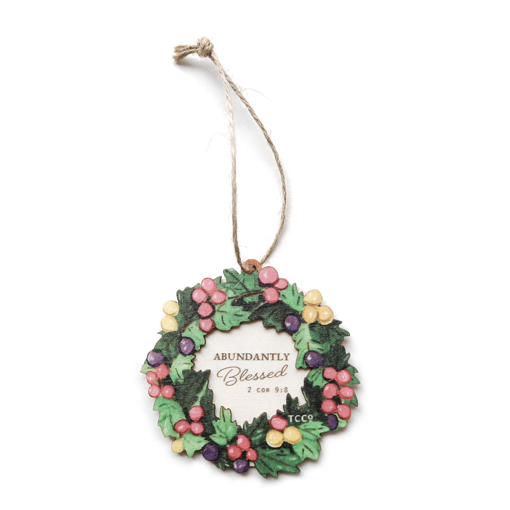 Decorative Christmas ornament featuring a colorful wreath with berries and the text 'Abundantly Blessed' from 2 Corinthians 9:8, perfect for spiritual holiday decor or faith-inspired gifts.