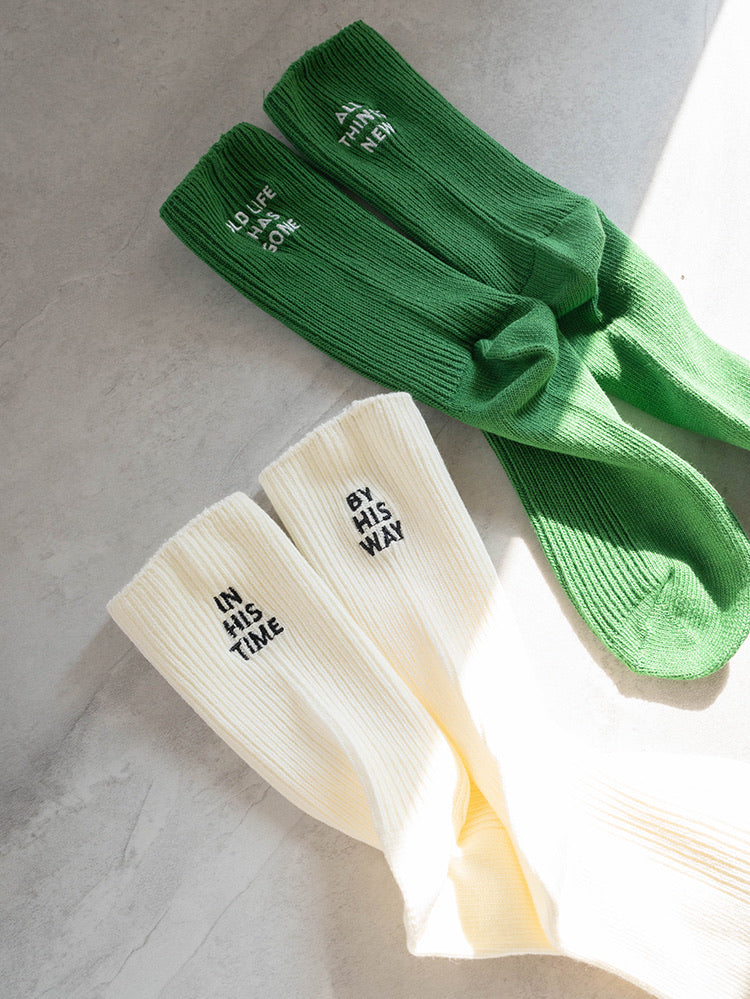 Cream and green ribbed-knit socks with embroidered messages—cream pair reads “IN HIS TIME” and “BY HIS WAY,” green pair reads “ALL THINGS NEW”—a faith-inspired accessory from The Commandment Co.