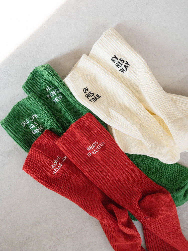 Multi-color ribbed-knit socks (white, green, red) with embroidered messages "IN HIS TIME," "BY HIS WAY," "ALL THINGS NEW," and "OLD LIFE HAS GONE"—a faith-inspired accessory from The Commandment Co.