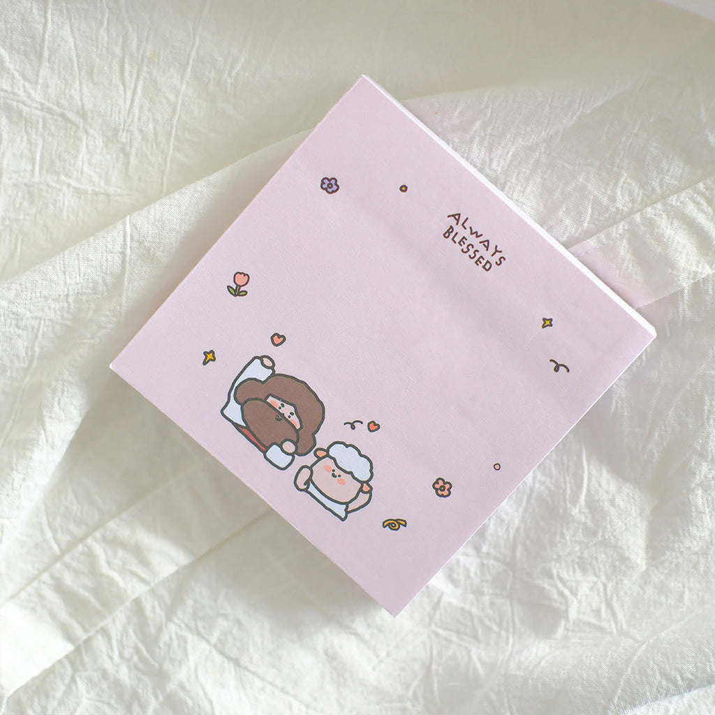 Pink sticky note featuring cute illustrations of Jesus and a sheep surrounded by small flowers, with the phrase 'Always Blessed' at the top, designed for faith-inspired stationery.