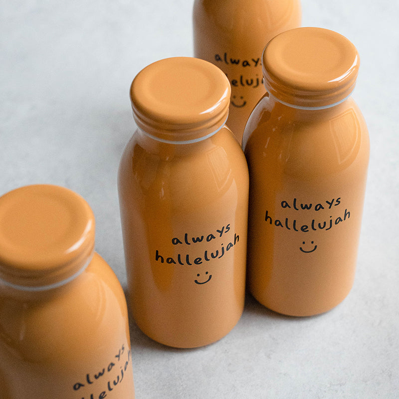 Mustard-colored milk bottle-shaped tumbler with the phrase "always hallelujah" and a smiley face