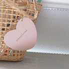 Heart-shaped keychain with 'Always Loved' engraved in gold, hanging on a wicker basket, showcasing a meaningful Christian gift in soft pink.