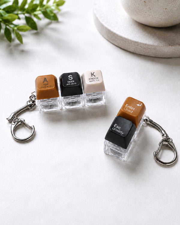 ASK SEEK KNOCK and Enter Christ Esc Anxiety light-up keycap keychains arranged on a white tabletop