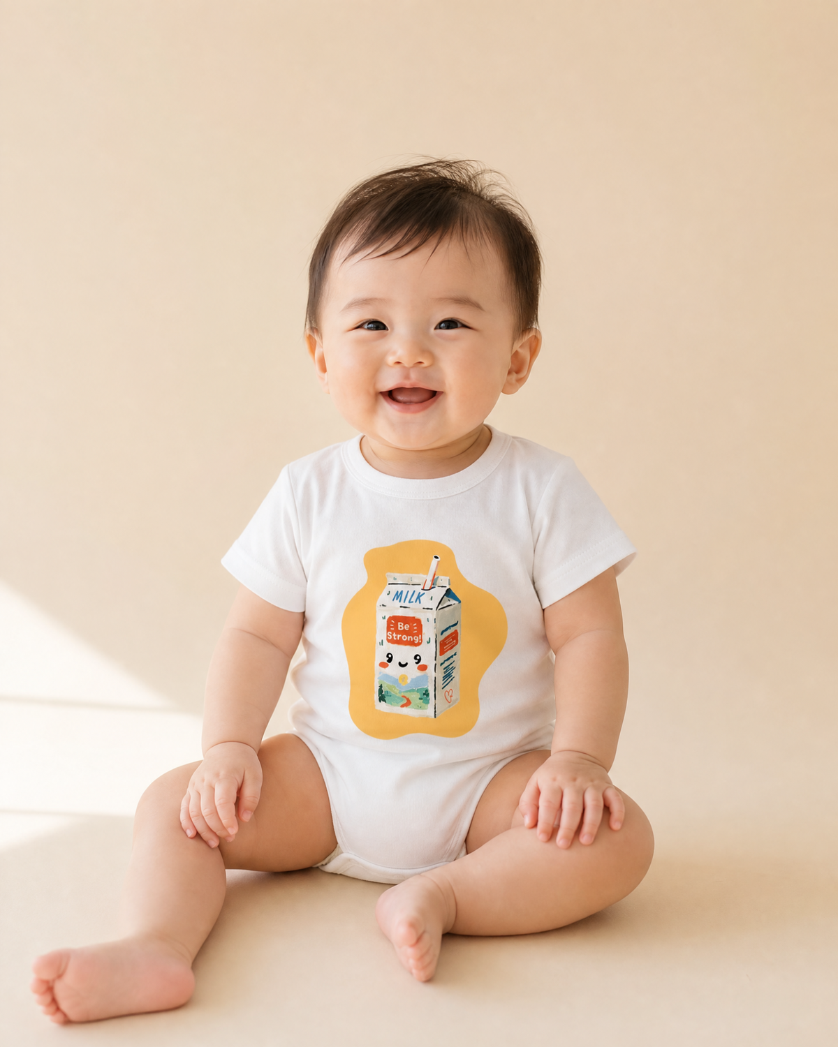 Smiling baby wearing a white Be Strong Milk romper with cheerful illustrated milk carton design