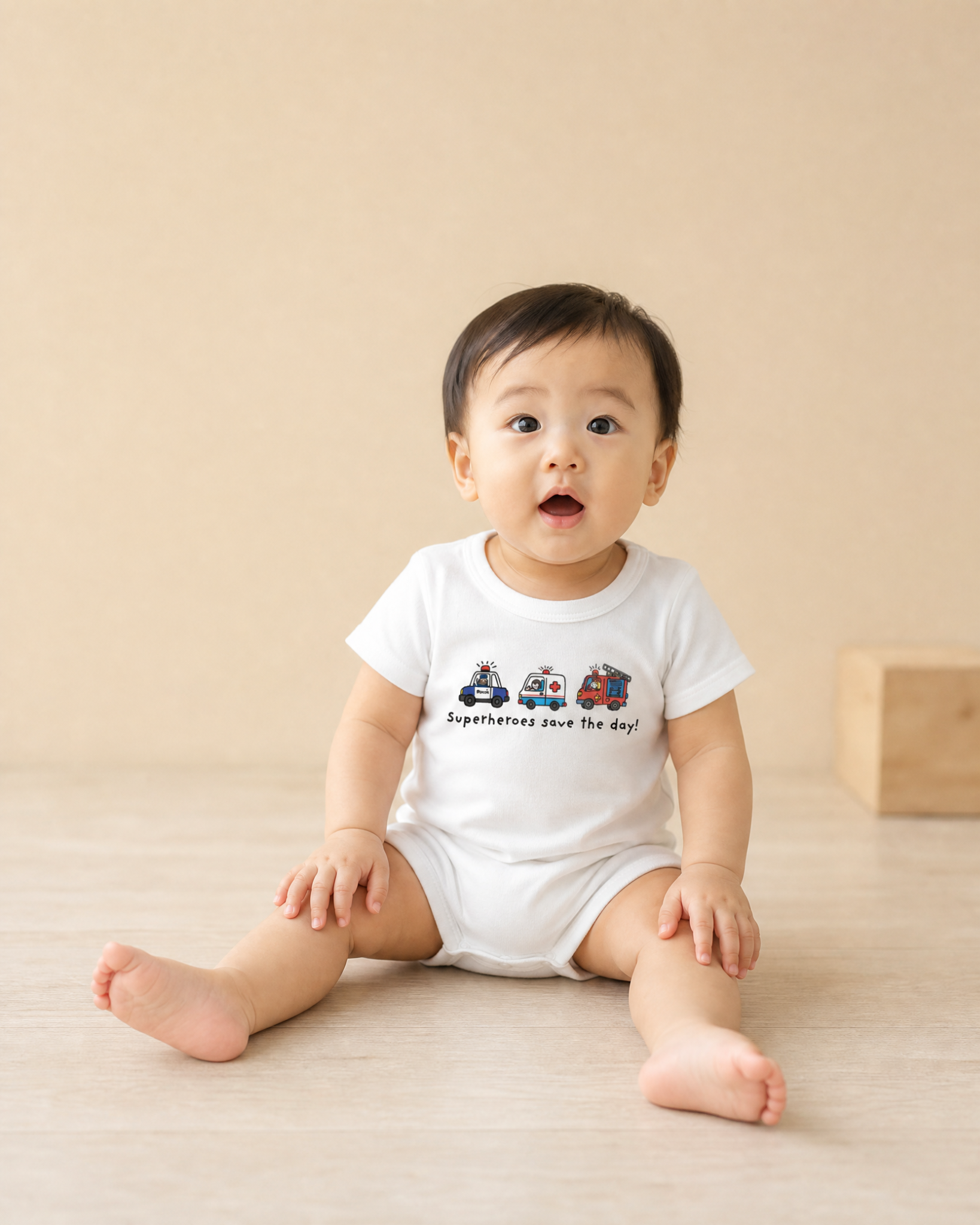 Smiling baby wearing a white Superheroes Save the Day romper with emergency vehicle illustrations