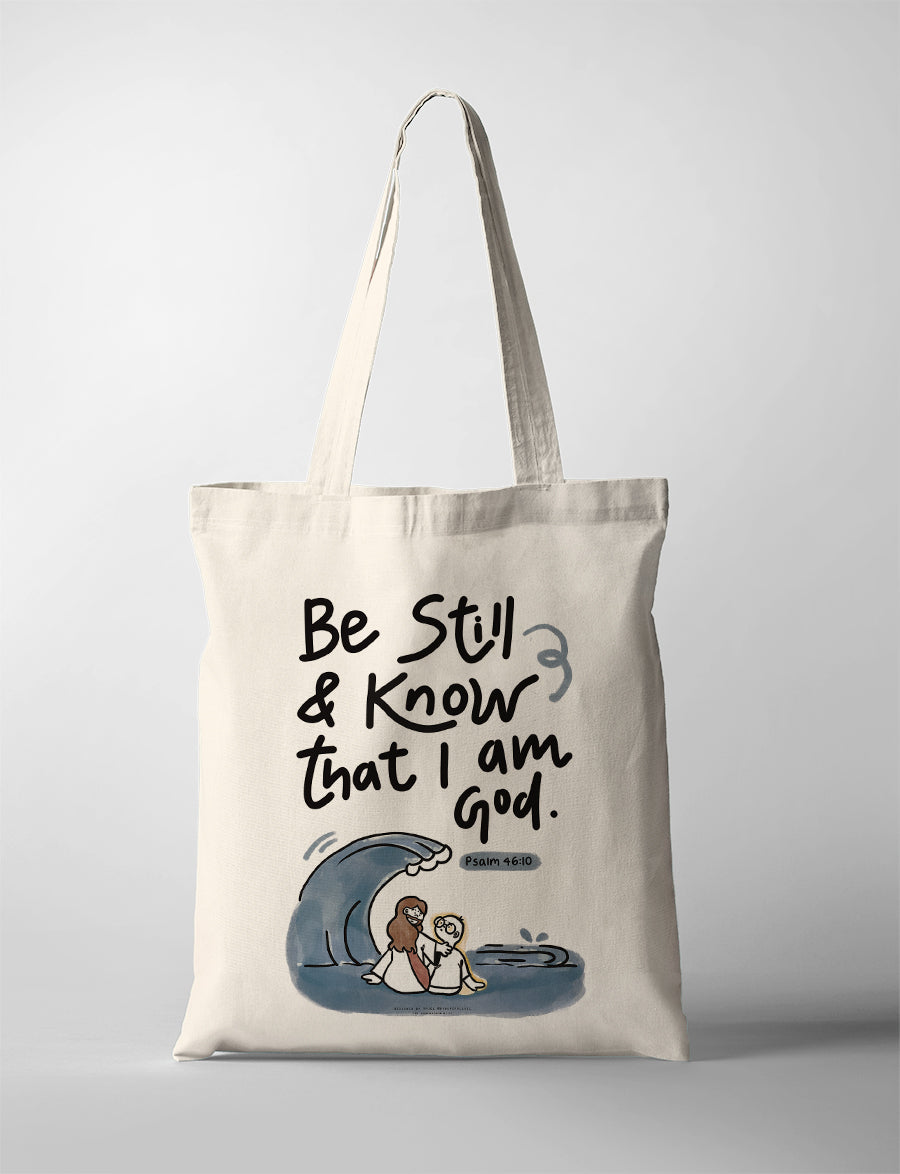 Cream canvas tote bag featuring “Be Still & Know That I Am God – Psalm 46:10” with illustrated wave and Jesus calming the storm design, Christian inspirational tote bag.