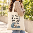Be Still and Know That I Am God Psalm 46:10 cream canvas tote bag being carried over the shoulder outdoors.