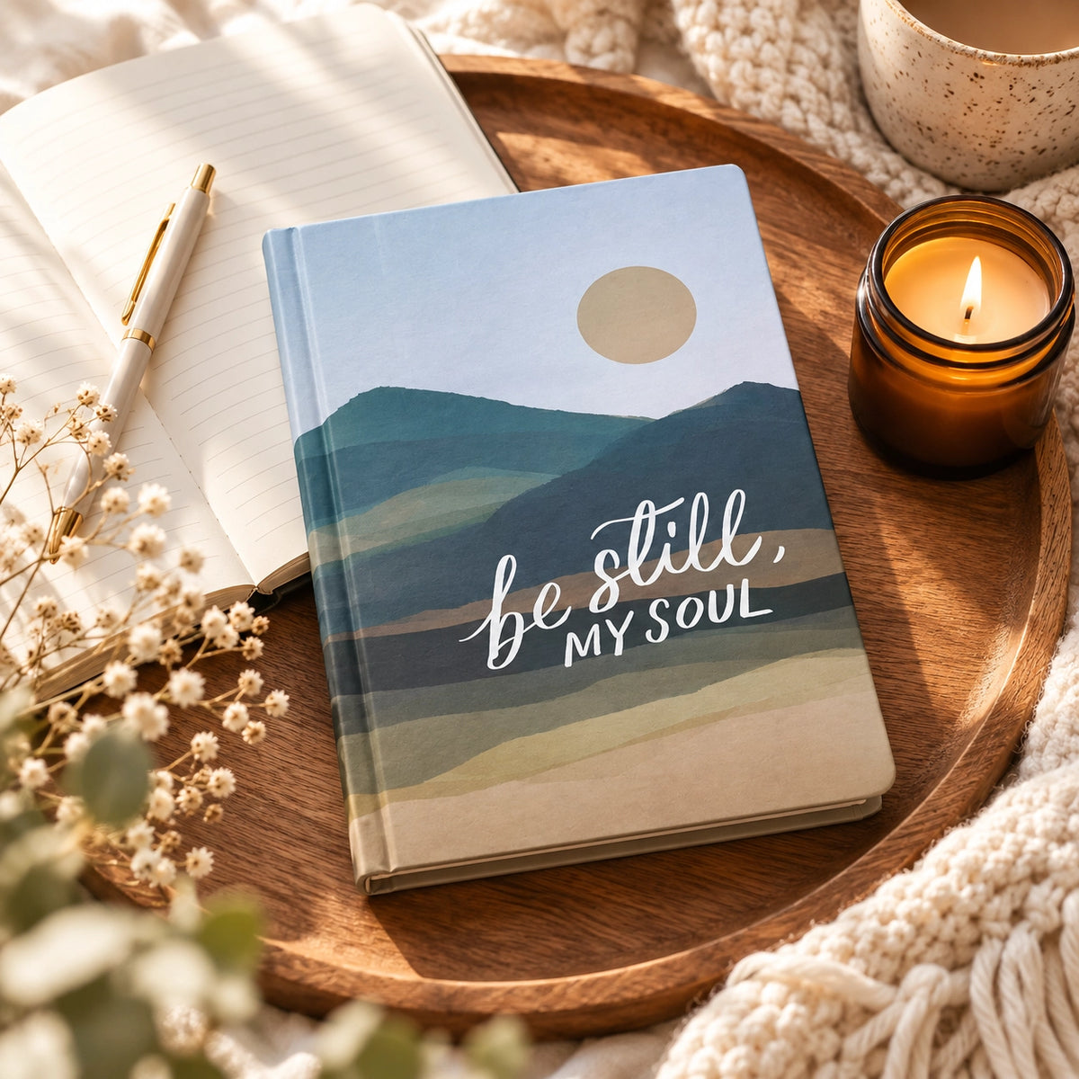 Be Still, My Soul Christian journal styled on a wooden tray with an open notebook, candle and soft neutral textiles.