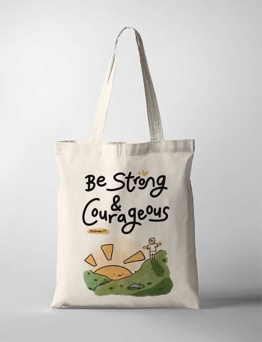 Cream canvas tote bag featuring “Be Strong & Courageous – Joshua 1:9” with a cute illustrated hill and child design, Christian inspirational gift.