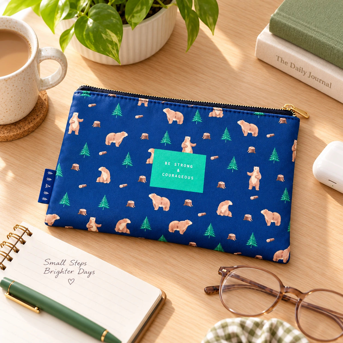 Be Strong and Courageous blue bear pattern pouch lying flat on a sunlit desk