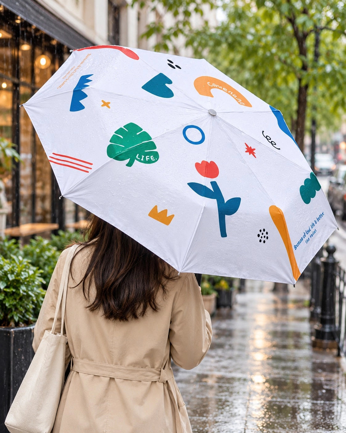 Because of God Life Is Better white umbrella with colourful Christian illustrations carried on a rainy city street.