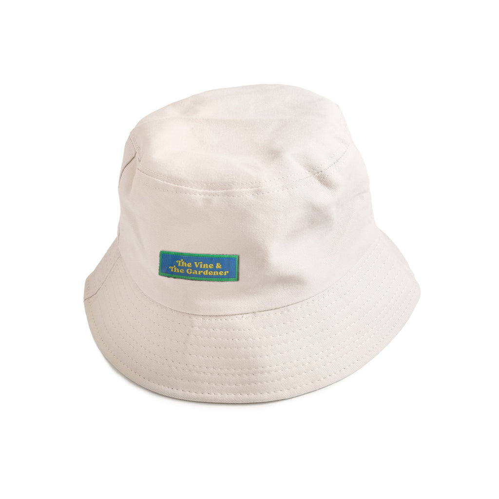 A beige bucket hat featuring a green patch with yellow text reading "The Vine & The Gardener," a Christian-inspired accessory with a faith-based message.