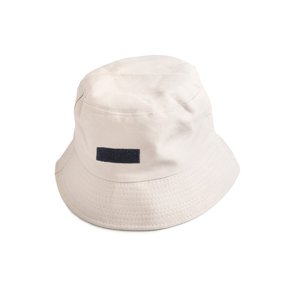 A beige bucket hat featuring a black velcro patch for customizable designs, offering a versatile and modern casual streetwear accessory.