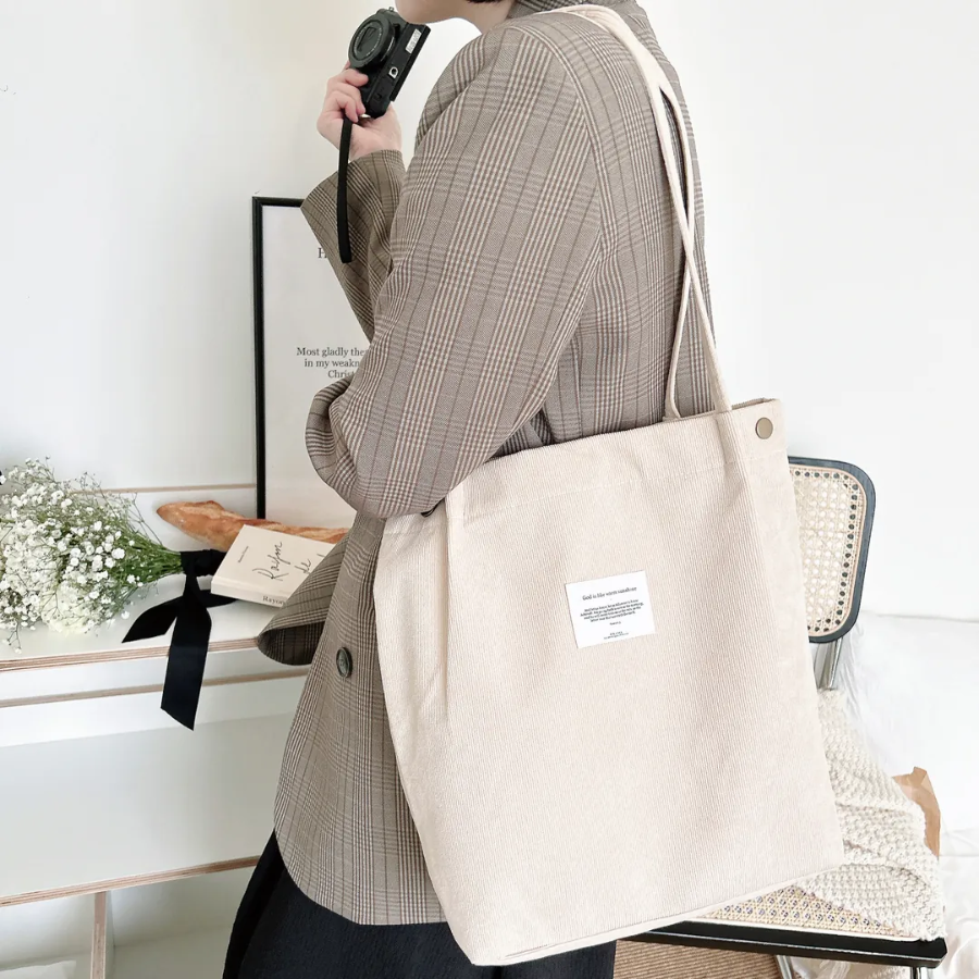 Woman carrying a beige corduroy shoulder bag with an inspirational patch, styled with a plaid blazer in a cozy, faith-inspired setting, reflecting simple happiness and everyday encouragement.