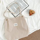 Beige corduroy shoulder bag with an inspirational patch, placed on a cozy white bed next to an open Bible and a plate with a scone, reflecting simple happiness and faith-inspired living.