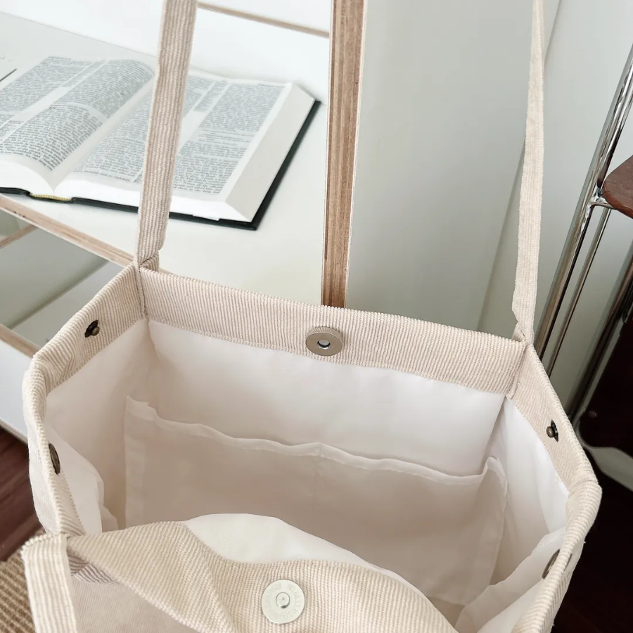 Interior view of a beige corduroy shoulder bag with white lining and inner pockets, highlighting its spacious and practical design for simple, faith-inspired living.