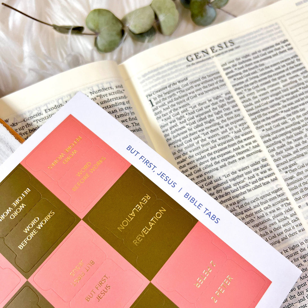 Open Bible showing the book of Genesis, alongside a set of pink and gold Bible tabs labeled 'Revelation' and '2 Peter,' with eucalyptus leaves in the background.