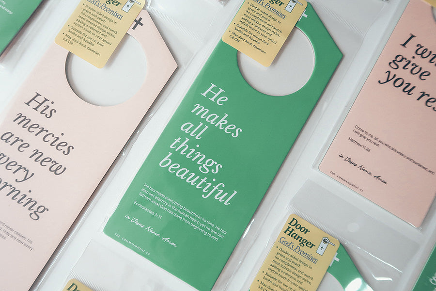 Close-up of Christian door hanger packaging featuring inspirational Bible verses such as 'He makes all things beautiful,' 'His mercies are new every morning,' and 'I will give you rest,' with a focus on God's promises.