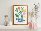 A beautifully crafted wooden poster featuring the Bible verse "Heaven & Earth, Sing Praises to You - Psalm 69:34." The design includes colorful floral and abstract cutouts, displayed on a white shelf adorned with minimalist vases and dried flowers for a modern and serene aesthetic.