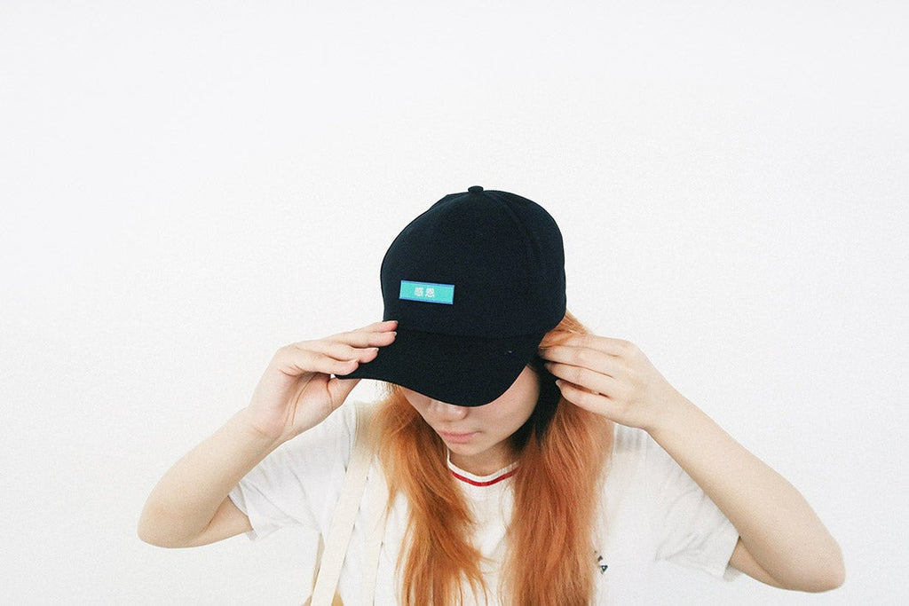 A person wearing a black cap with a turquoise velcro patch featuring the word "Gratitude" in Chinese, showcasing a faith-inspired and customizable streetwear accessory.