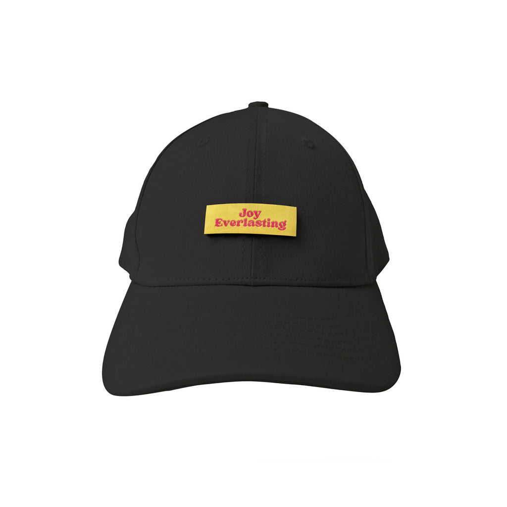 A black cap featuring a yellow patch with red text reading "Joy Everlasting," a Christian-themed headwear piece conveying positivity and faith.