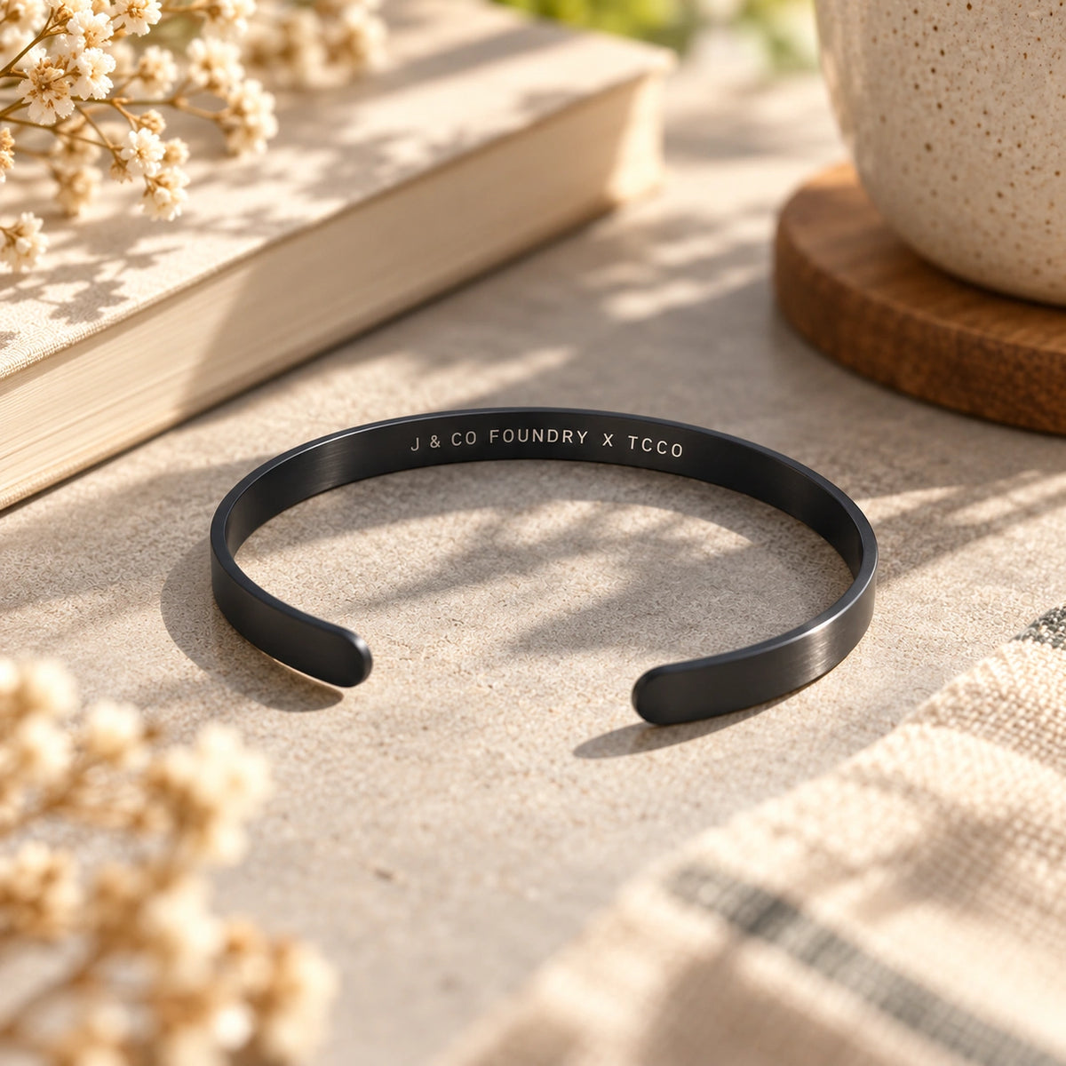 Black stainless steel open cuff band with J and Co Foundry X TCCO engraving on its inside