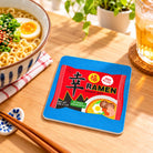 Blessed Ramen Christian coaster styled beside a bowl of ramen and drink on a bright dining table.