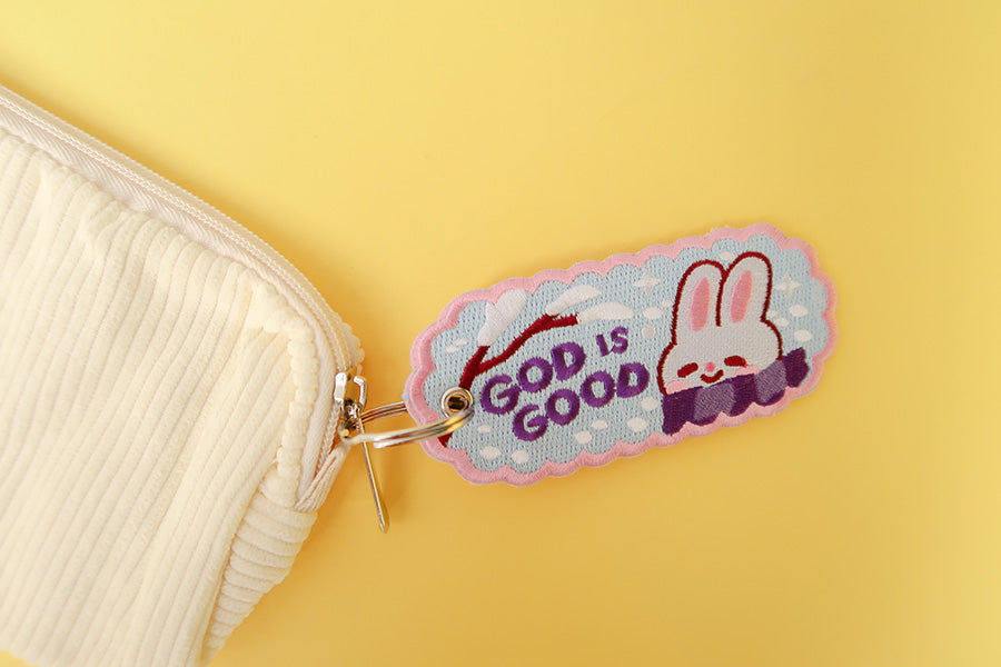 Cute blue embroidered keychain with a smiling white bunny and the text 'GOD IS GOOD'.