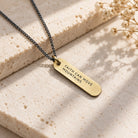 Brass bar necklace engraved Faith Can Move Mountains styled on a neutral stone surface