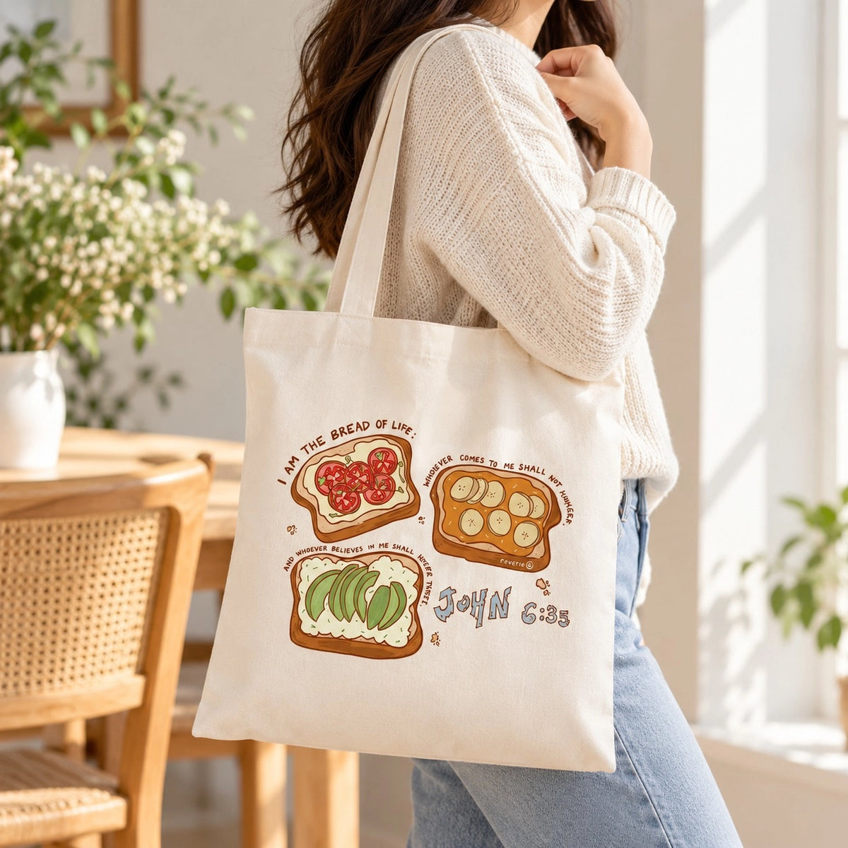 Bread of Life John 6:35 cream canvas tote bag with illustrated toast designs worn over the shoulder indoors.
