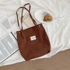  Brown corduroy shoulder bag with an inspirational patch, displayed on a cozy white bed alongside open books, a plate with a scone, and a Bible, reflecting simple happiness and faith-filled living.