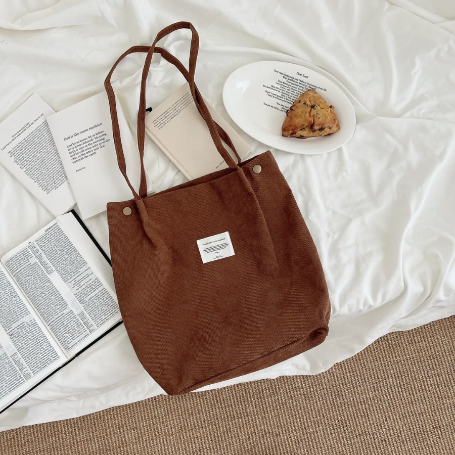  Brown corduroy shoulder bag with an inspirational patch, displayed on a cozy white bed alongside open books, a plate with a scone, and a Bible, reflecting simple happiness and faith-filled living.