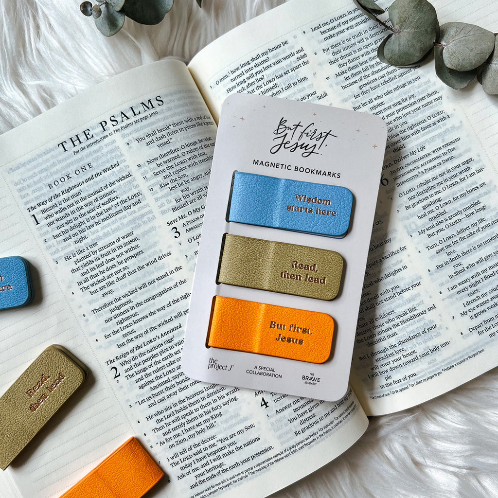 Set of three magnetic bookmarks labeled 'Wisdom starts here,' 'Read, then lead,' and 'But first, Jesus,' placed on an open Bible turned to Psalms with eucalyptus leaves on a white fluffy background.