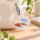 Cai Peng Abundant Blessings acrylic keychain hanging from a cream pouch in a bright lifestyle setting