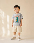 Young child wearing the grey RAAAW dinosaur kids T-shirt with beige shorts