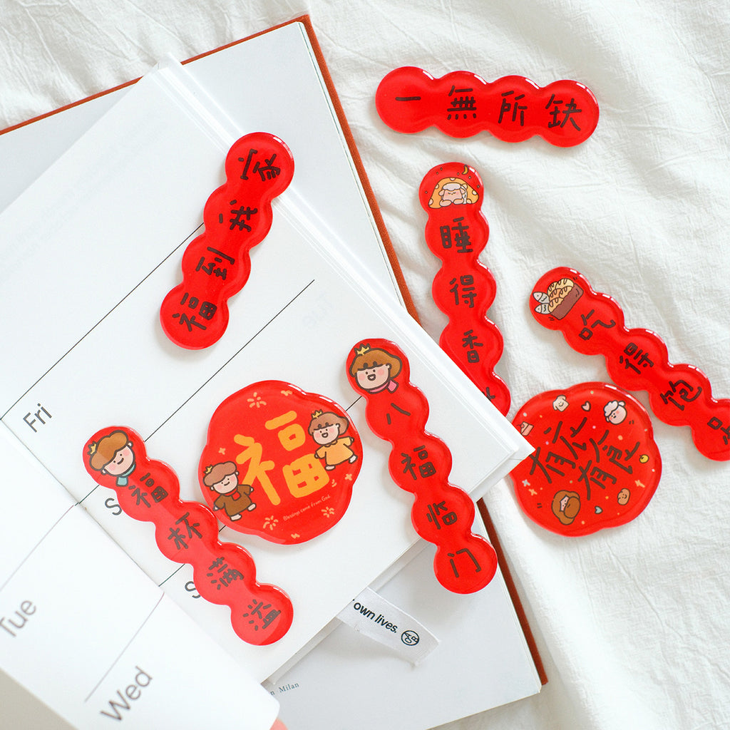 A set of Chinese New Year red couplet magnets with festive designs, blessings, and playful illustrations displayed on an open planner