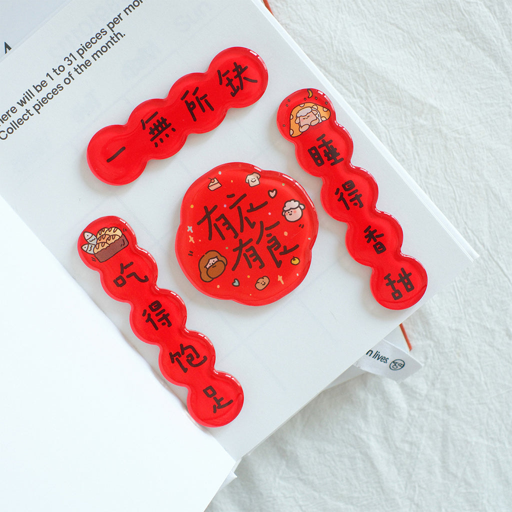 Set of red Chinese New Year couplet magnets with blessings, featuring cute illustrations and characters, displayed on an open planner.