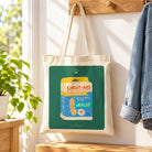 Christ-aid Love Bandages canvas tote bag on a wooden peg in a sunlit home entryway.