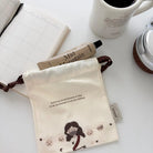 God Loves Us canvas drawstring pouch with a Jesus and sheep illustration, styled with a planner, coffee and everyday essentials