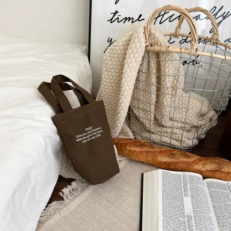 Brown Christian canvas drink carrier bag styled with a Bible, bread, and cosy home decor