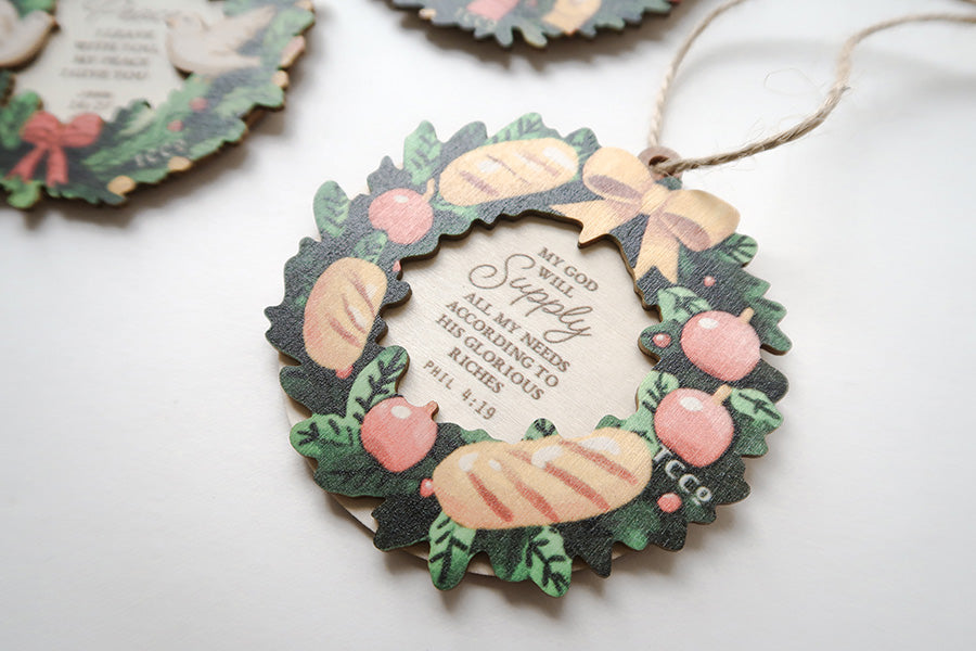 Close-up of a Christian Christmas wreath ornament featuring the Bible verse Philippians 4:19, decorated with bread, and apples