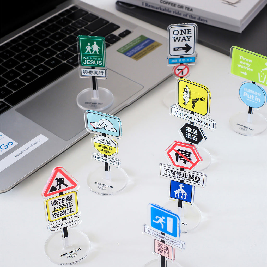 A collection of Christian acrylic desk signs featuring messages like 'Walk with Jesus,' 'Put God First,' 'One Way Follow Jesus' and more, placed on a desk next to a laptop, promoting faith and encouragement.