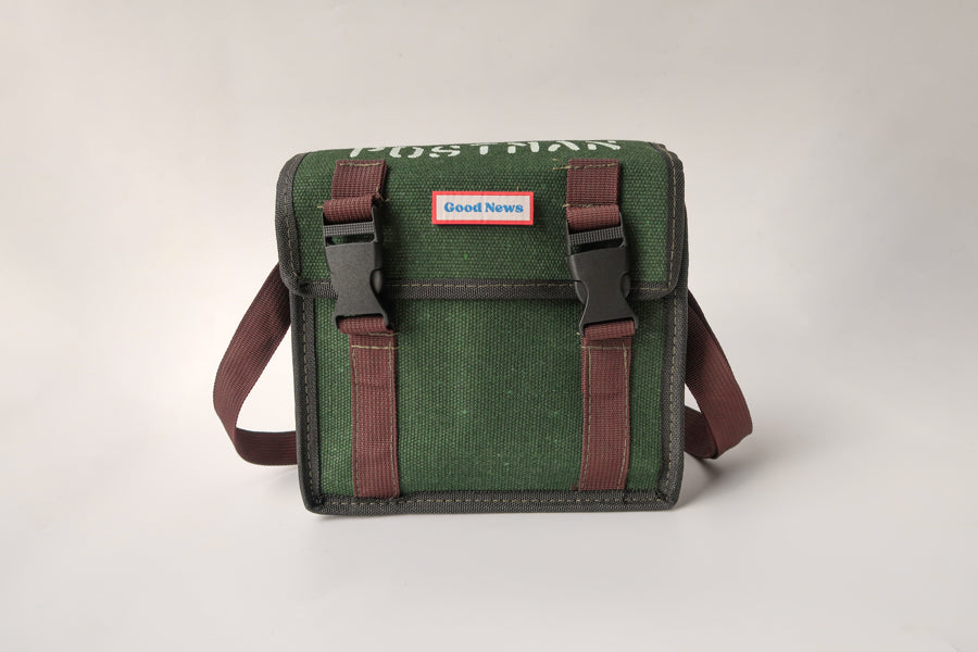 A green canvas messenger bag with 'Good News' branding on the front, featuring brown straps and a durable design. The bag is faith-themed with a minimalist, rugged look suitable for daily use.