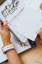  Hands holding a page from The Project J Christian notepad featuring the encouraging verse "Do not be afraid, for I am with you" from Isaiah 41:10, surrounded by faith-inspired planners and notes for uplifting daily organization.