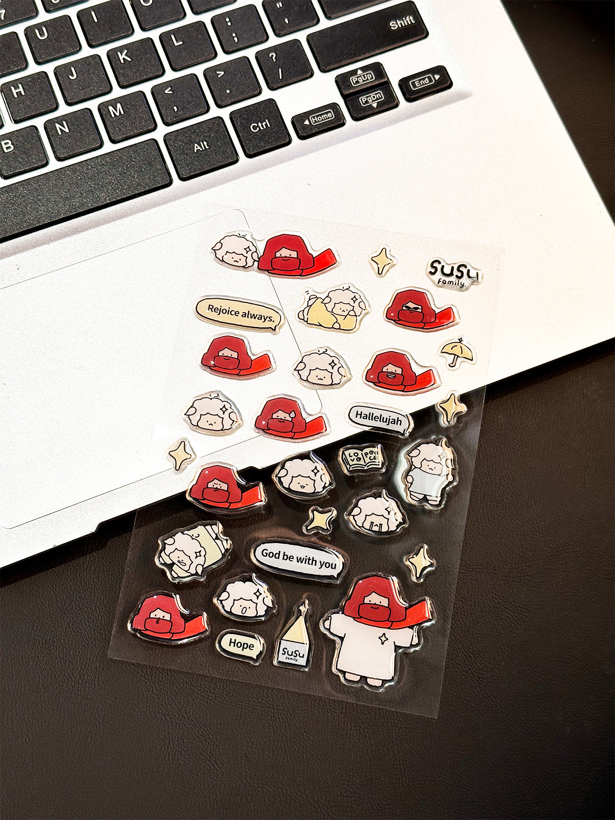 Cute Christian stickers on laptop featuring kawaii Jesus and sheep with Bible verse phrases like rejoice always and hallelujah