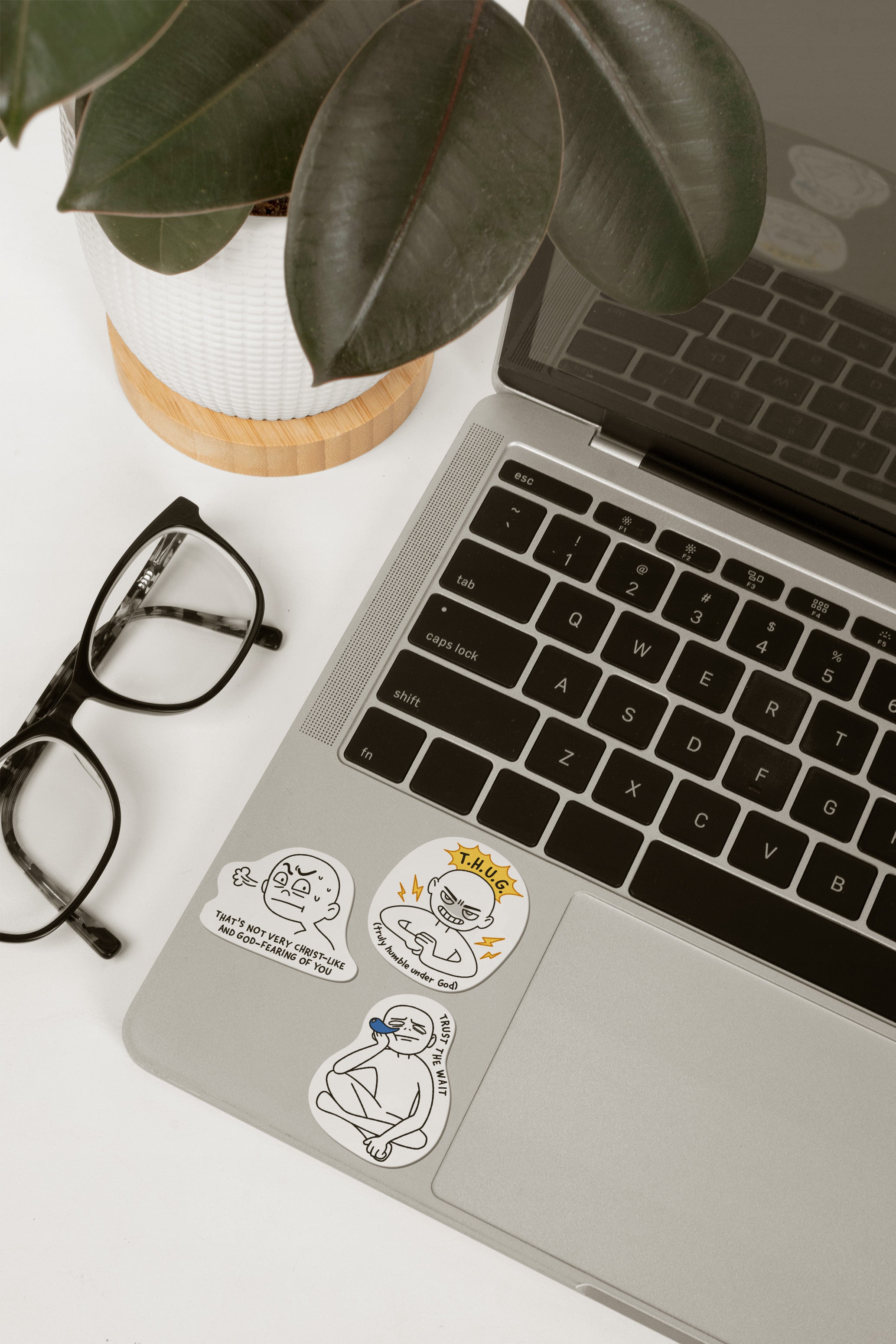 Laptop adorned with humorous Christian stickers featuring messages like "Trust the wait," from The Commandment Co, Singapore