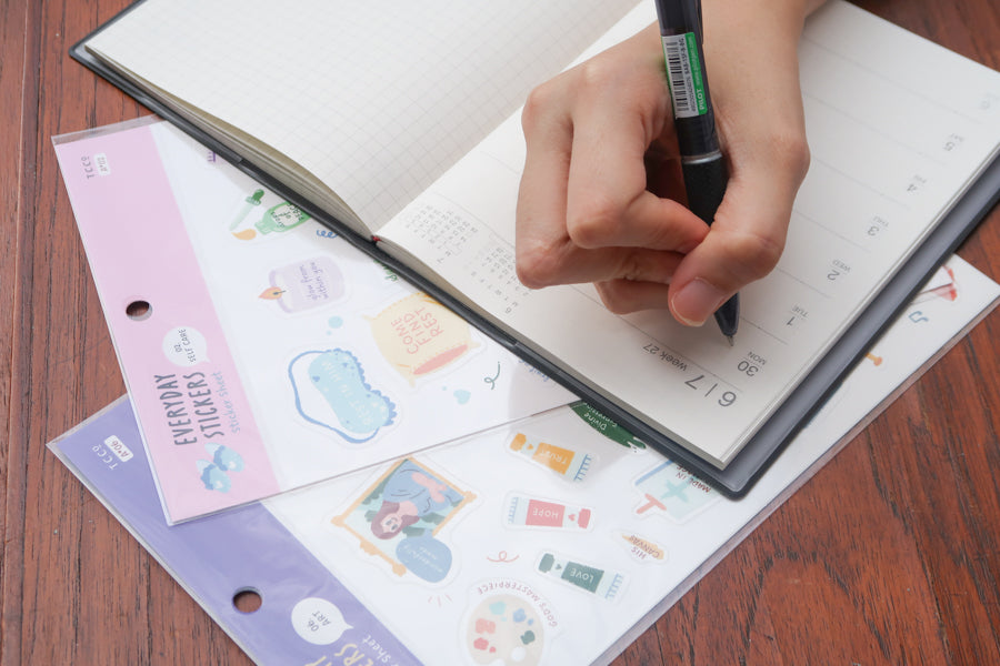Hand placing a cute Christian sticker from everyday believer sticker sheet onto a planner, showing journaling and faith-inspired sticker use