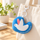 Come Holy Spirit dove plushie keychain clipped to a cream canvas bag